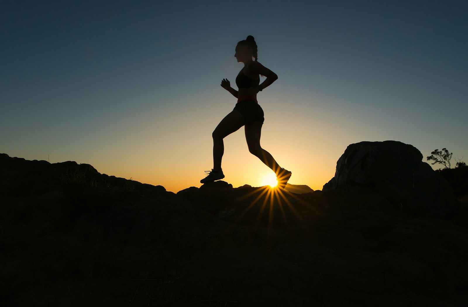 silhouette of man jumping on rocky mountain during sunset